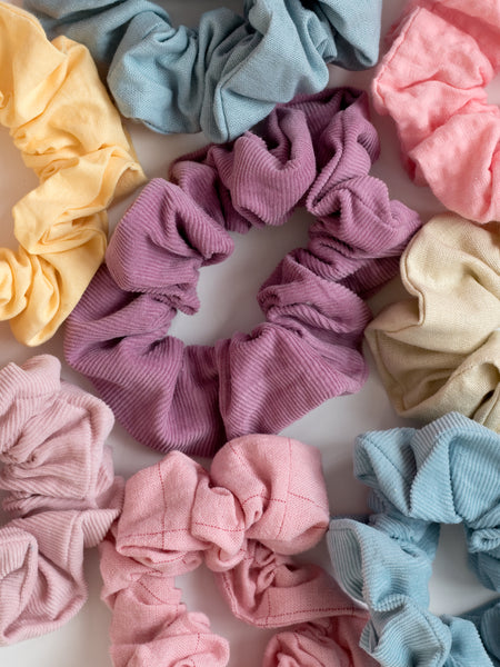 A close-up of many pastel scrunchies tightly packed next to each other on a white wooden floor.