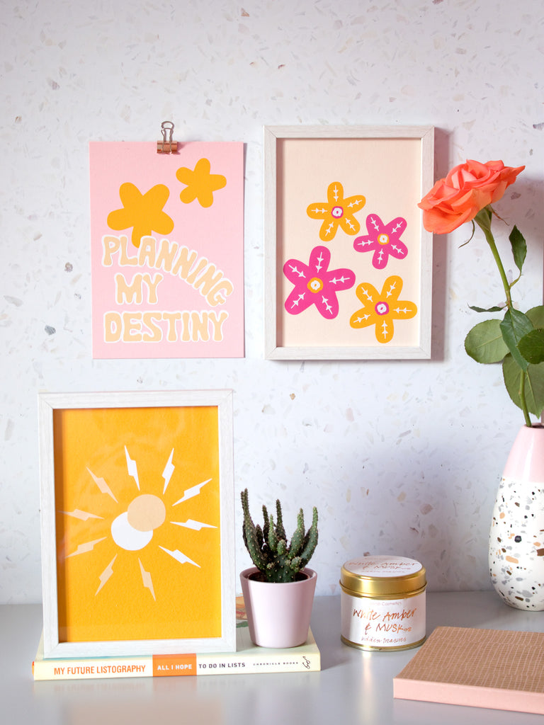 Two art prints are displayed on the wall. One is framed, sitting on top of a book on a table. The table is styled with flowers and candles.