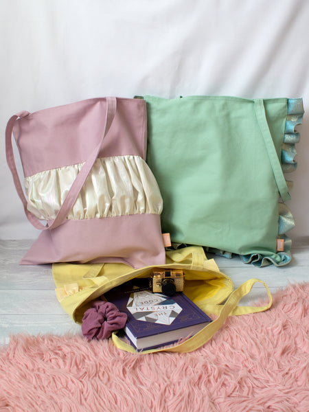 Three different coloured tote bags lay on a white wooden floor. 