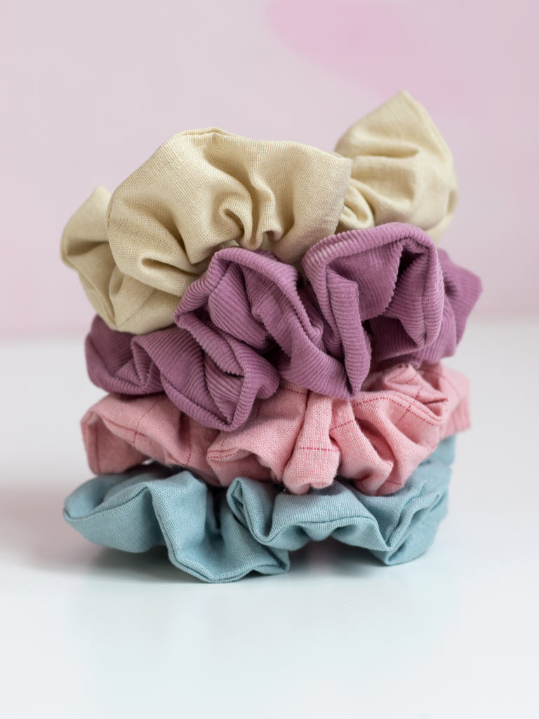 Four different coloured pastel scrunchies are placed on top of each other on a pink foreground.