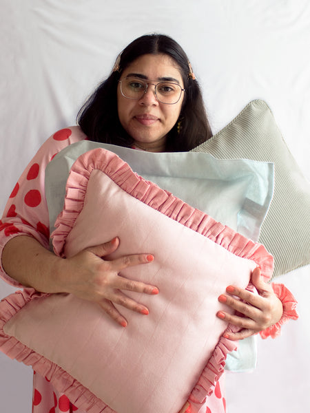 A female holding three different coloured cushions in her arms and simpling in front of a white background.
