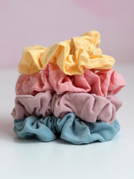 Four different coloured pastel scrunchies are placed  on top of each other on a pink foreground.