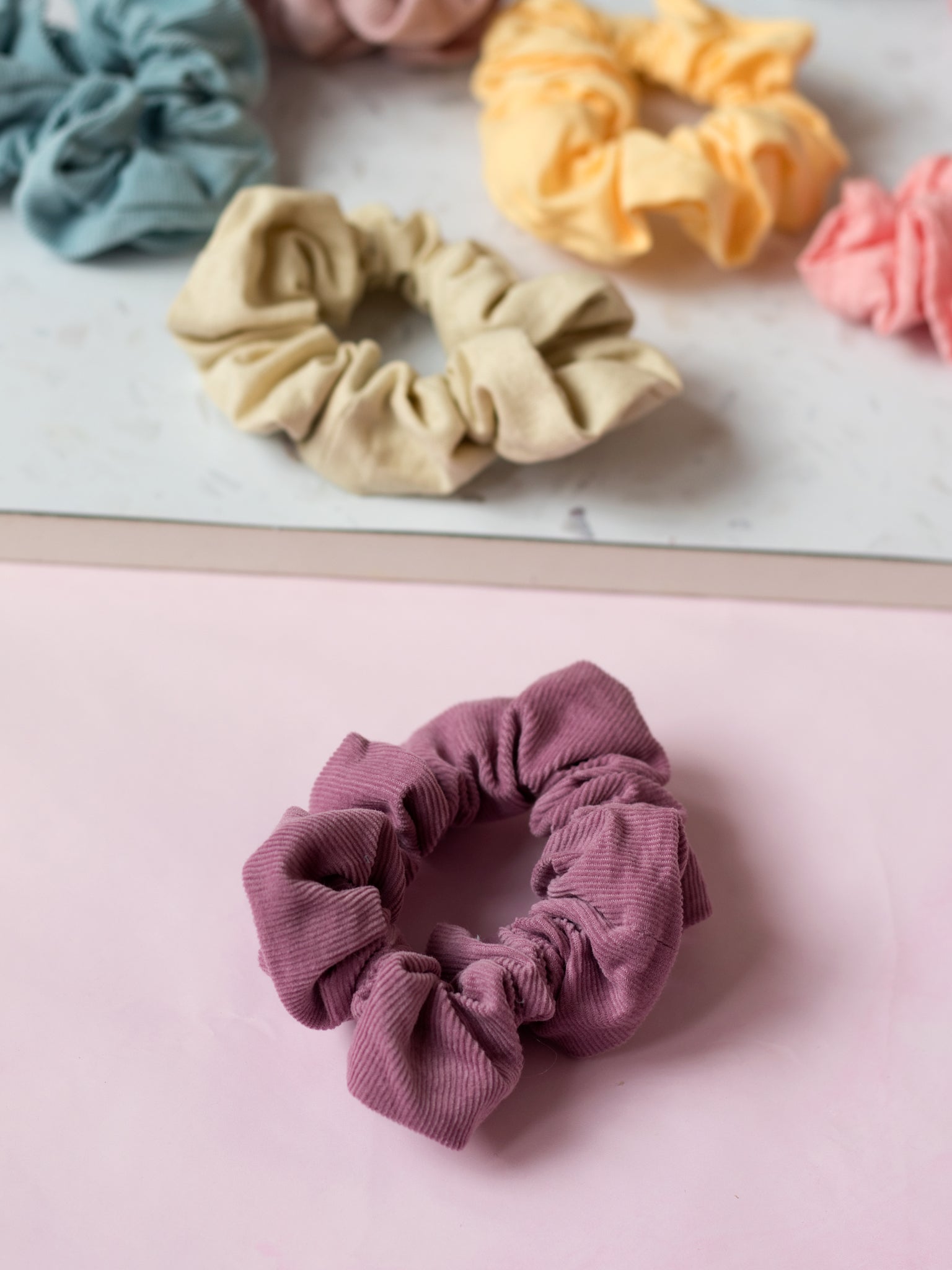 Different coloured pastel scrunchies are placed next to each other on a terrazzo and pink tabletop. 
