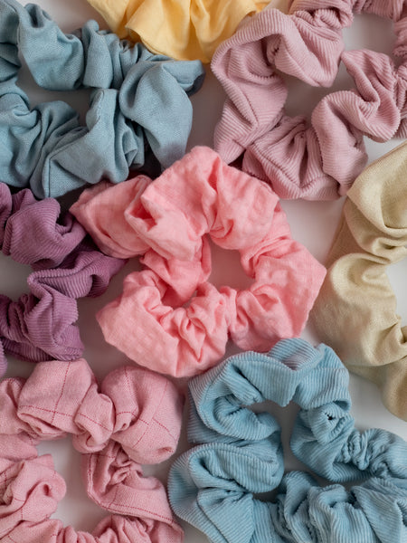 A close-up of many pastel scrunchies tightly packed next to each other on a white wooden floor.