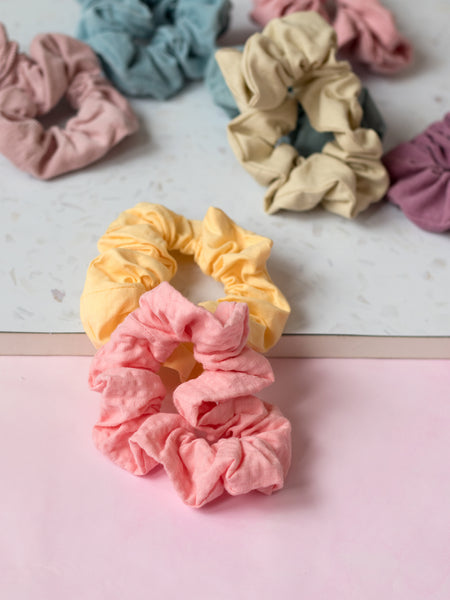 Different coloured pastel scrunchies are placed next to each other on a terrazzo and pink tabletop. 