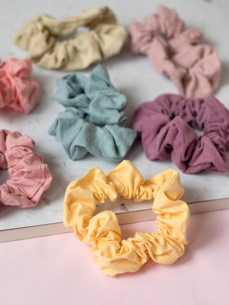Different coloured pastel scrunchies are placed next to each other on a terrazzo and pink tabletop. 