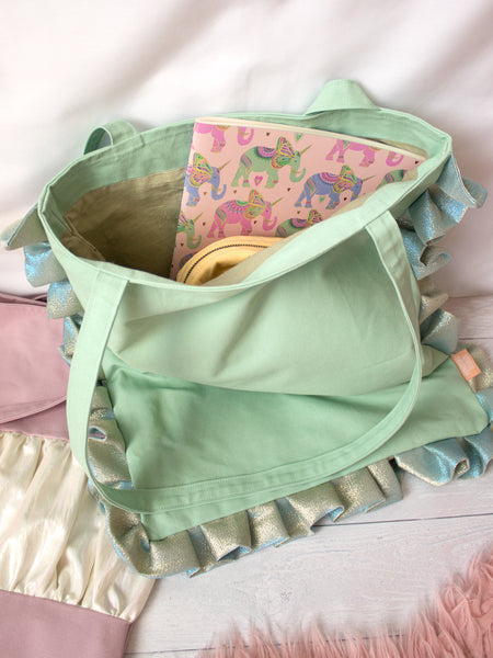 A mint green ruffle tote bag is open on the floor showing its content of a notepad and a yellow makeup bag.