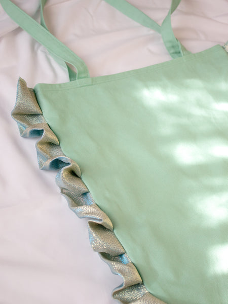 Close-up details of a mint green tote bag with shiny green ruffles along the edge.