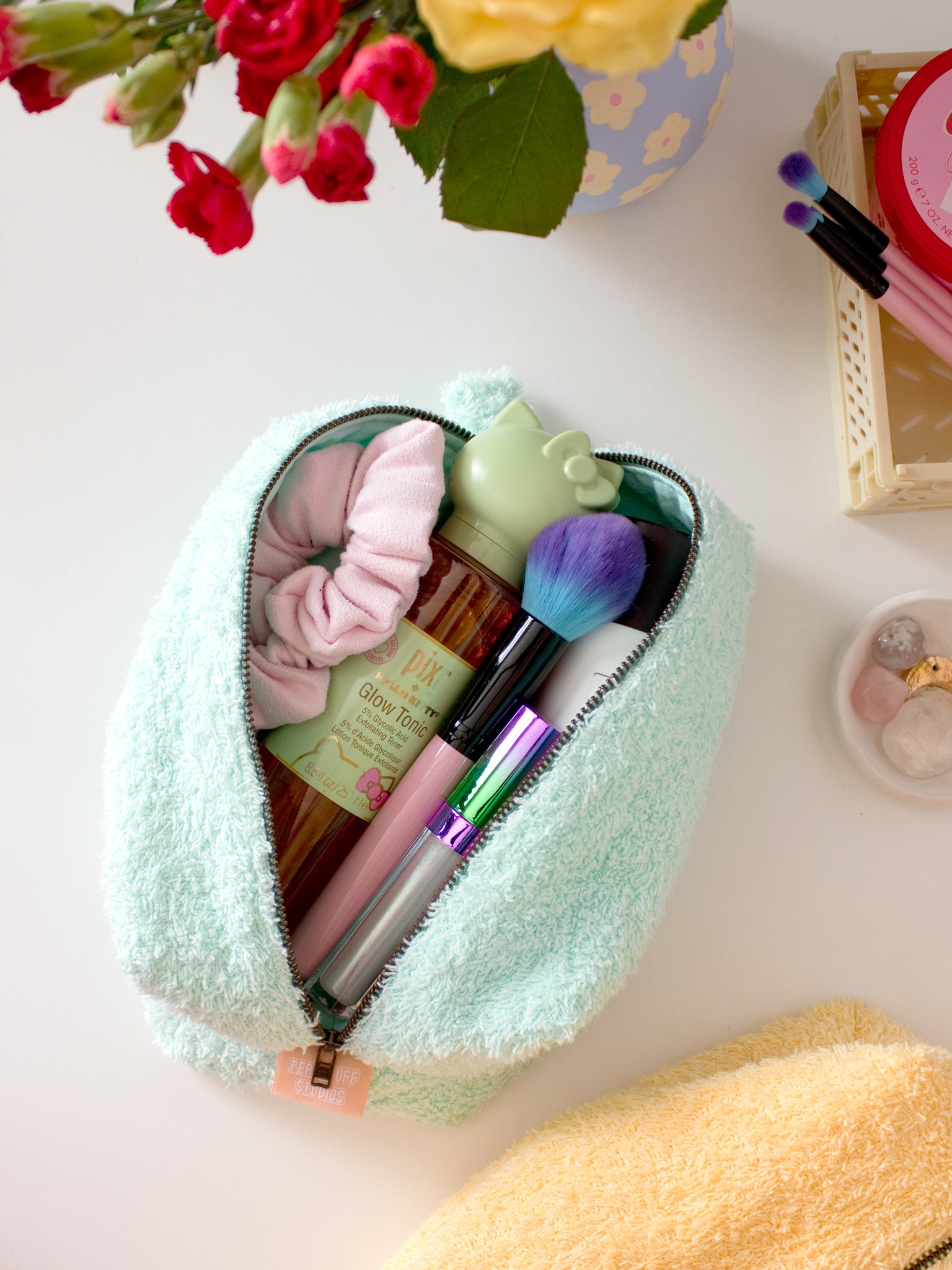 A mint green towelling makeup bag on a table, open to reveal beauty products.