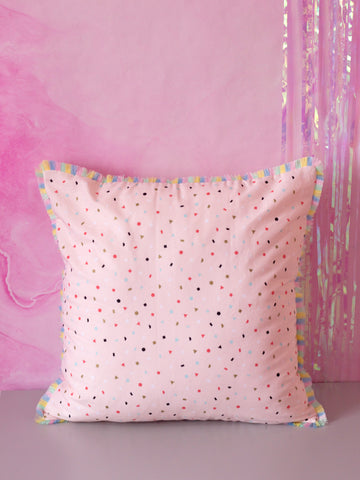 A pink cushion with pastel rainbow fringe in front of a marbled pink wall. 