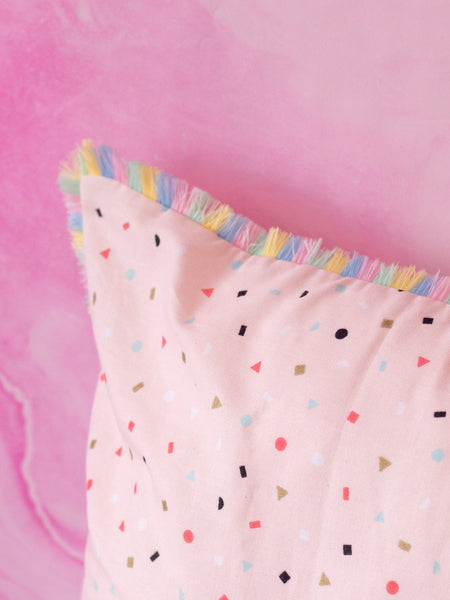 A close-up of a pink cushion with pastel dots shows the pastel rainbow fringe trim.