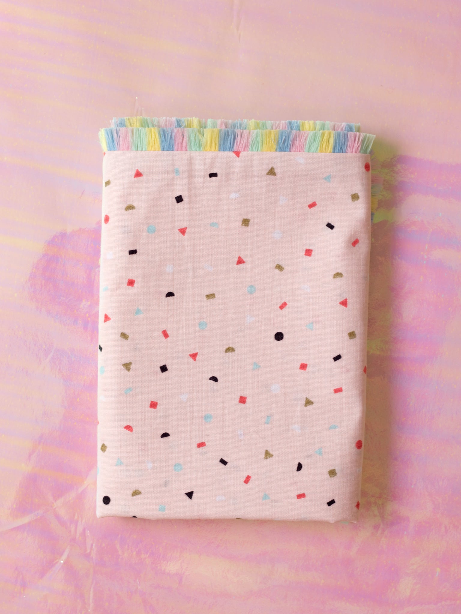 A pink cushion with pastel rainbow fringe folded on an iridescent background.