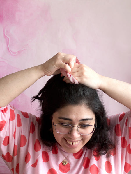 A female tying a pink checked cotton scrunchie around the top of her hair. 