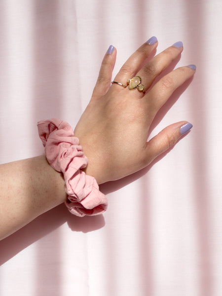 A pink checked cotton scrunchie on a female wrist, who is wearing a ring and purple nail varnish.