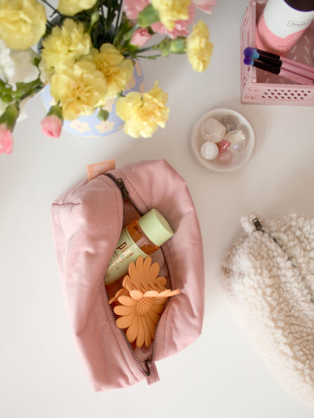 A pink corduroy makeup bag on a table, open to reveal beauty products.