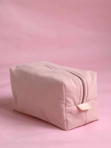 A pink corduroy makeup bag on a pink marbled foreground.