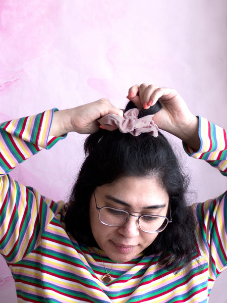 A female tying a pink corduroy scrunchie around the top of her hair. 