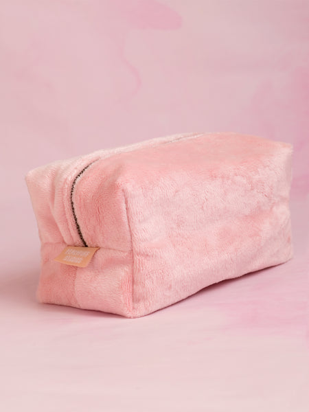 A pink plush makeup bag on a pink marbled foreground.