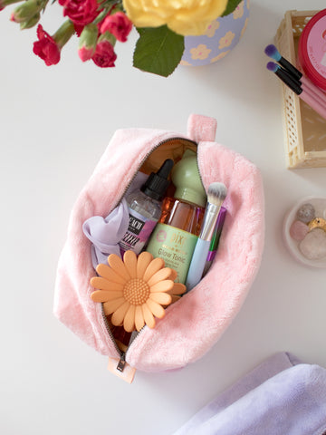 A pink plush makeup bag on a table, open to reveal beauty products.