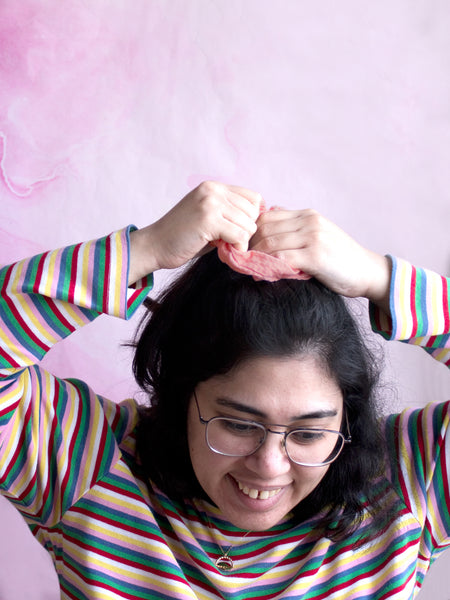 A female tying a pink organic cotton seersucker scrunchie around the top of her hair. 