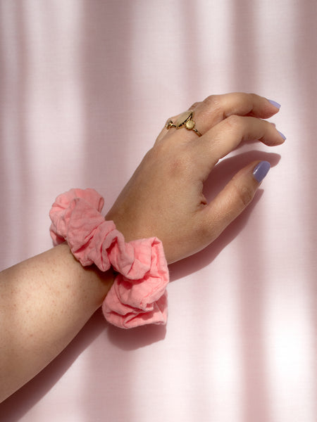 A pink organic cotton seersucker scrunchie on a female wrist, who is wearing a ring and purple nail varnish.