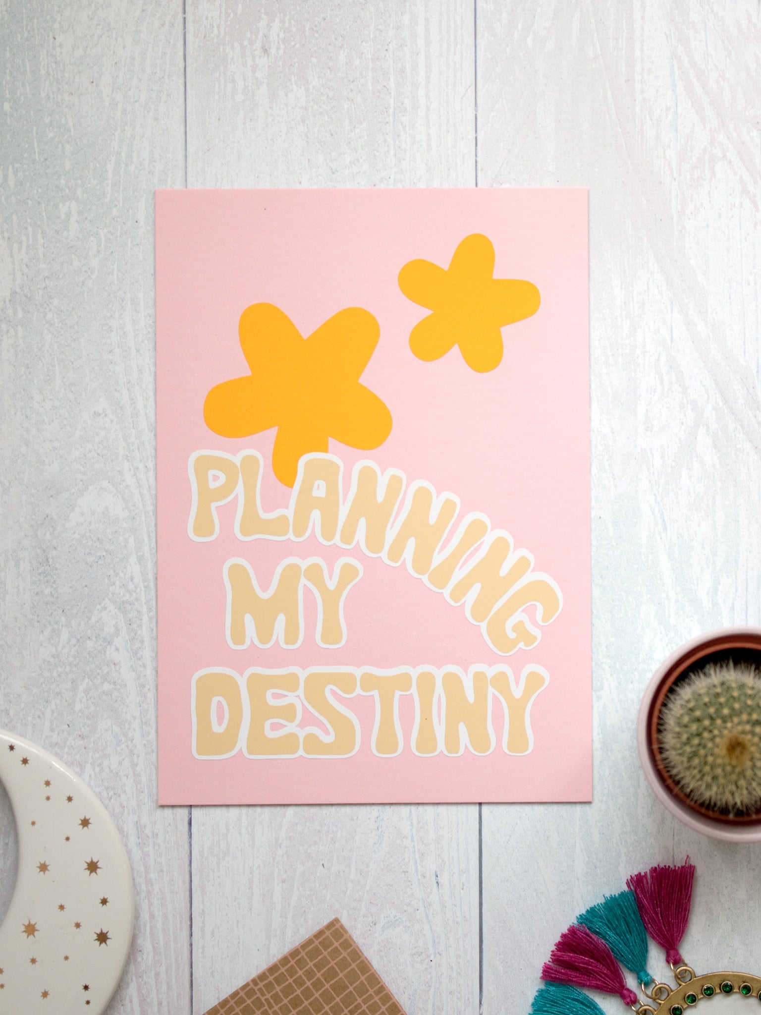 Planning My Destiny art print lay on a white wooden floor. Trinkets and a cactus lay offset at the bottom.