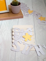 A paper letter garland wrapped around a cardboard backing that's placed on a white wooden floor.