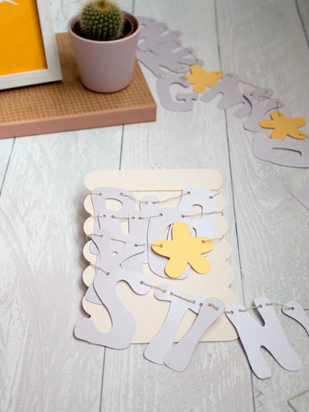 A paper letter garland wrapped around a cardboard backing that's placed on a white wooden floor.