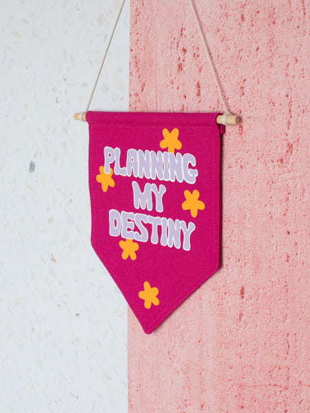 A pink canvas banner that reads Planning My Destiny with purple lettering is hung on a white and pink textured wall.