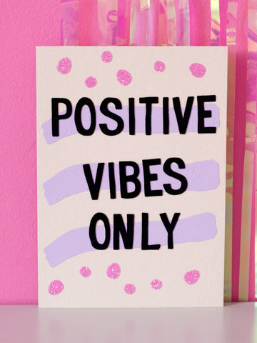 Art print with Positive Vibes Only in flocked font written over three purple strips and pink glittery dots, sitting in front of a pink wall.