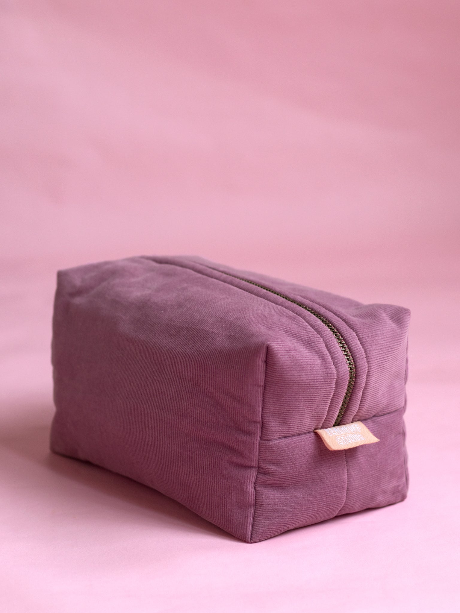 A purple corduroy makeup bag on a pink marbled foreground.