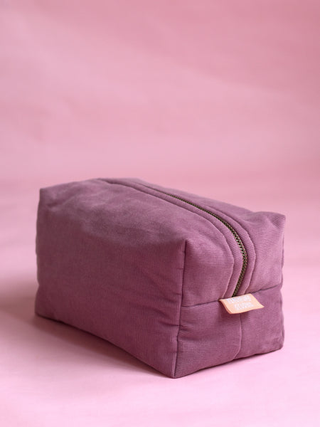 A purple corduroy makeup bag on a pink marbled foreground.