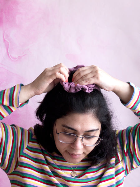 A female tying a purple corduroy scrunchie around the top of her hair. 