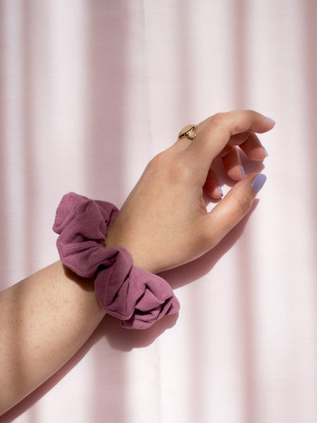 A purple corduroy scrunchie on a female wrist, who is wearing a ring and purple nail varnish.