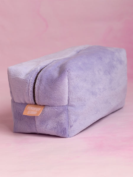 A purple plush teddy makeup bag on a pink marbled foreground.