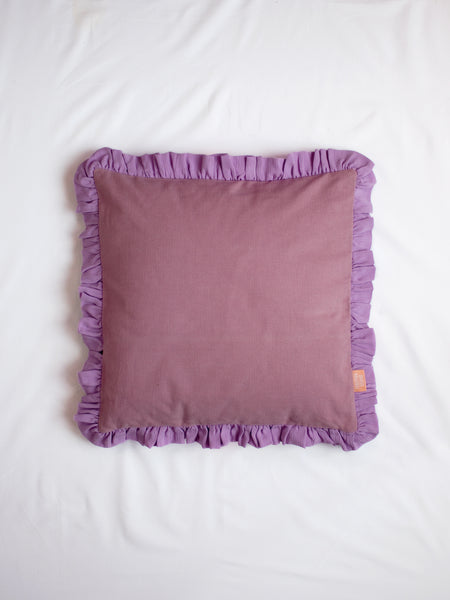 A purple ruffle cushion on the centre of a white bedsheet.
