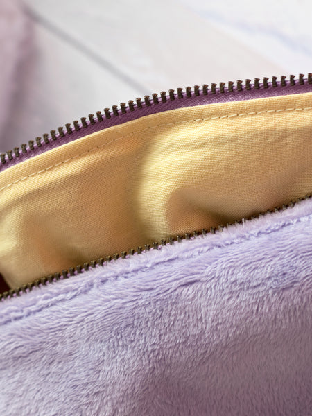 A close-up detail of a purple plush makeup bag with a yellow lining.