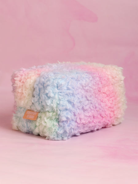 A rainbow fluffy makeup bag on a pink marbled foreground.