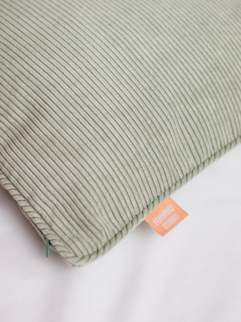 A close-up of a sage green corduroy cushion cover to show the pipping and ribbed details.