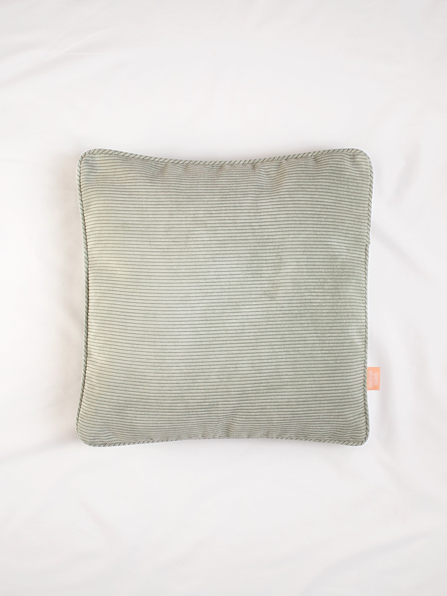 A sage green corduroy cushion on the centre of a white bedsheet.