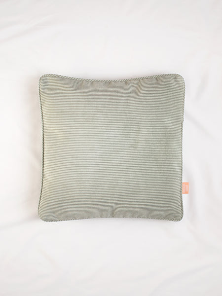 A sage green corduroy cushion on the centre of a white bedsheet.