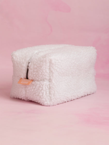 A white fluffy makeup bag on a pink marbled foreground.