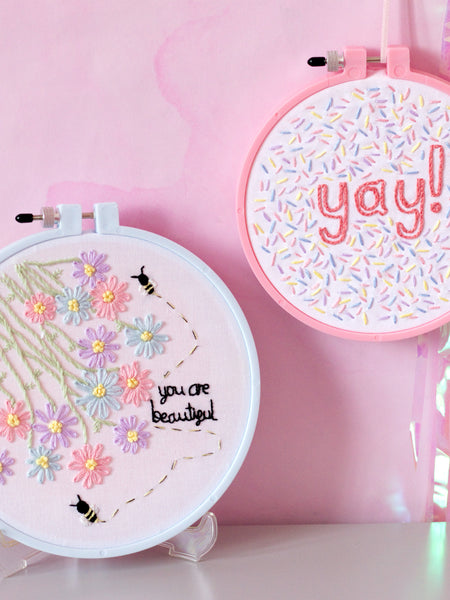 A pink embroidery hoop hung on the wall and a blue embroidery hoop displayed on the table.