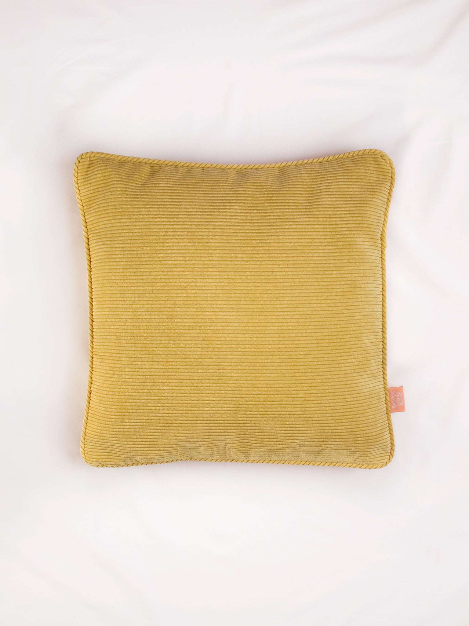 A yellow corduroy cushion on the centre of a white bedsheet 