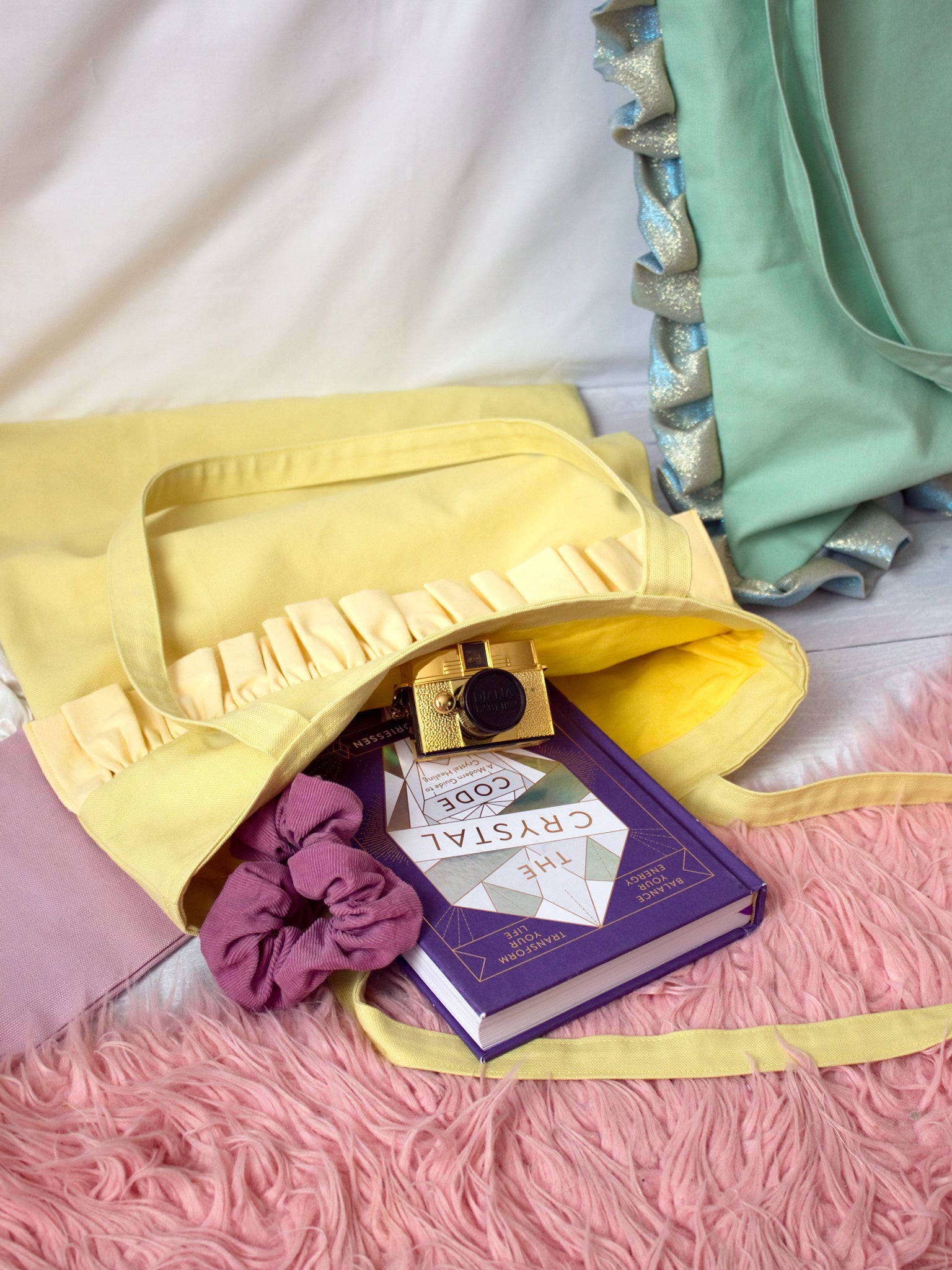 A yellow ruffle tote bag is open on the floor, showing the contents of a notepad, scrunchie and camera.