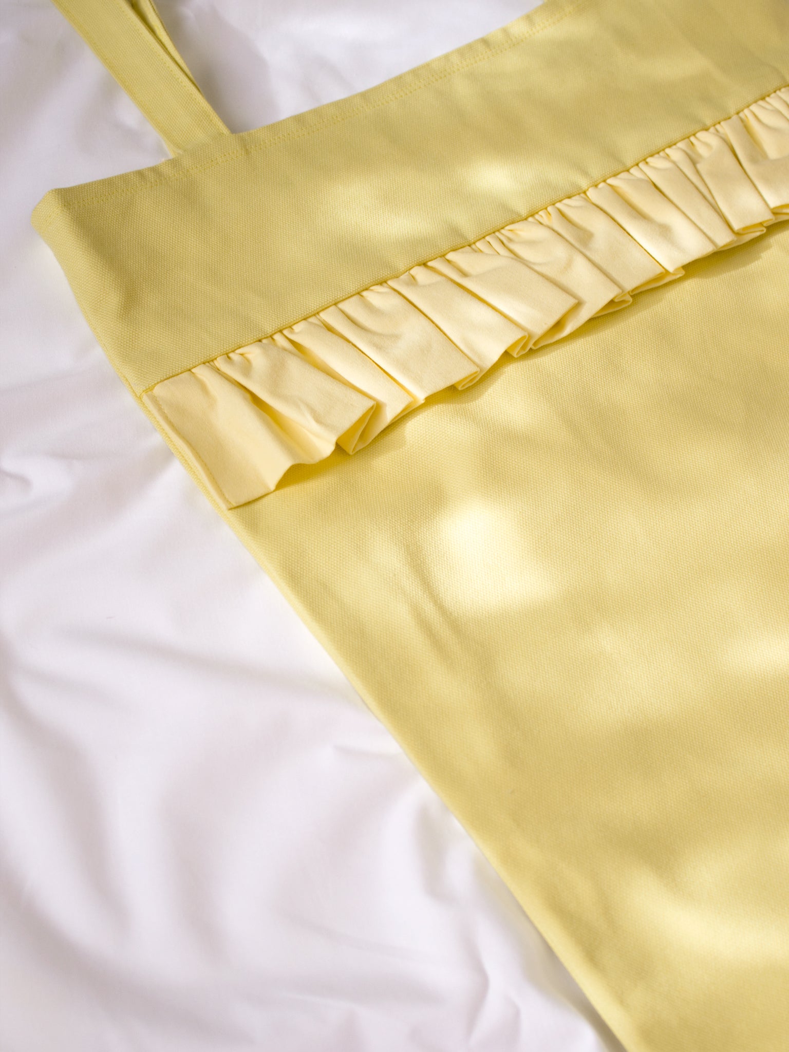 Close-up details of a yellow tote bag with a ruffle across the top.