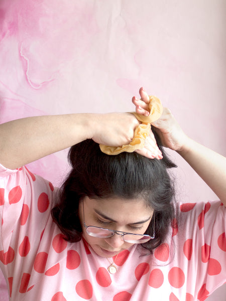 A female tying a yellow cotton scrunchie around the top of her hair. 