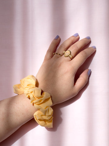 A yellow cotton scrunchie on a female wrist, who is wearing a ring and purple nail varnish.