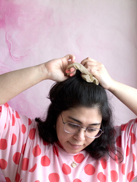 A female tying a yellow linen scrunchie around the top of her hair. 