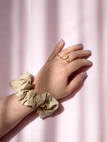 A yellow linen scrunchie on a female wrist, who is wearing a ring and purple nail varnish.